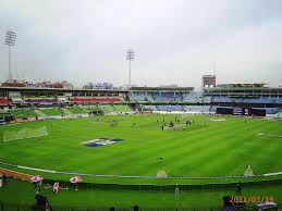 Panoramic view of Mirpur Cricket Stadium with green pitch, stands, and players in action.